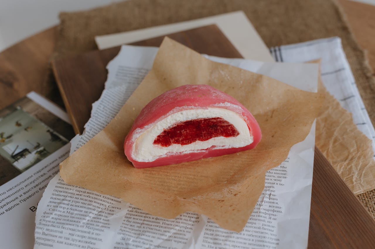 Close-up of a pink strawberry mochi dessert on rustic paper, showcasing its texture.